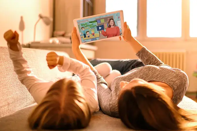 A mom and child lay side by side watching a financial education video on a tablet.