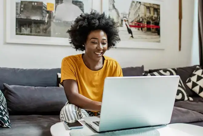 A woman sits on living room sofa while working on her laptop