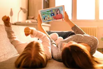 A mom and child lay side by side watching a financial education video on a tablet.
