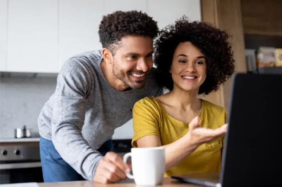 A couple smiles while looking at a laptop
