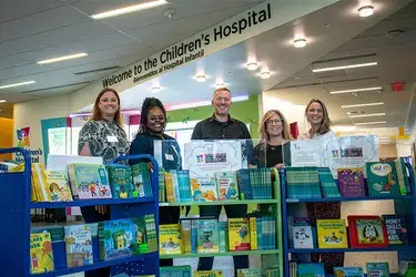 VACU team smiling while gathered around a bookshelf of children's books