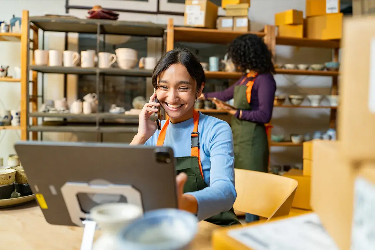 Business owner talks on the phone at a shop while looking at a computer