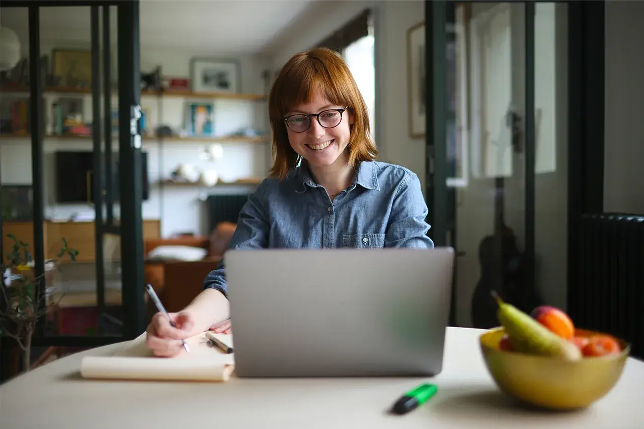 Women smiling while sitting at a table working on her laptop