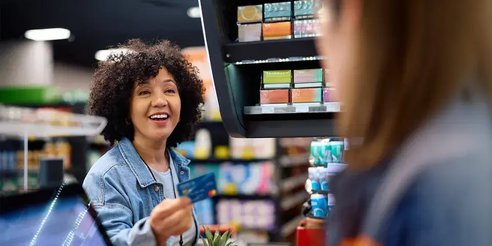 Women smiles with credit card in hand while checking out at grocery store.