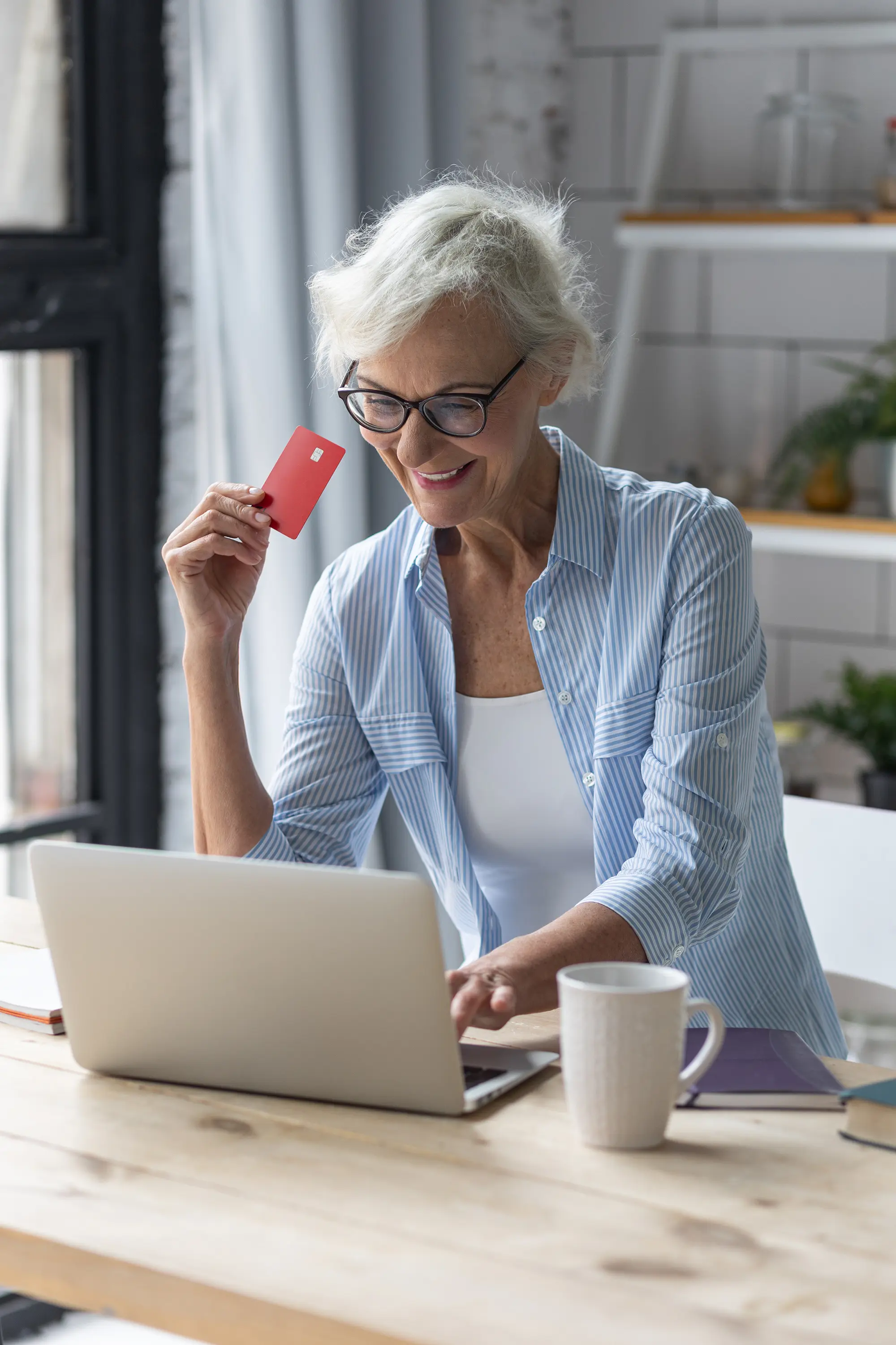 Adobe Stock 510102416 Beautiful senior woman with short grey hair and lovely smile shopping in the internet at home with a credit card Concept of mature woman using technology copy