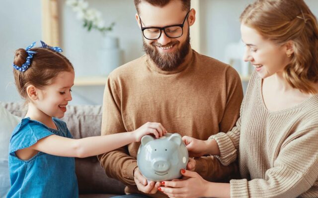 Mother and father watch young daughter put money into piggy bank 978b8d064138018a1dfad71b9882dd21
