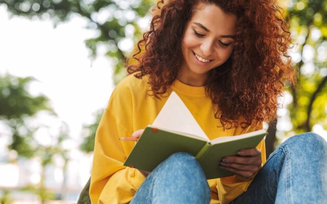 Young female college student writes in notebook while sitting outside on campus 978b8d064138018a1dfad71b9882dd21