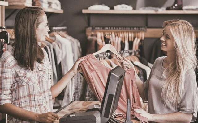 Young woman at clothing store checkout hands shirt to sales associate 978b8d064138018a1dfad71b9882dd21