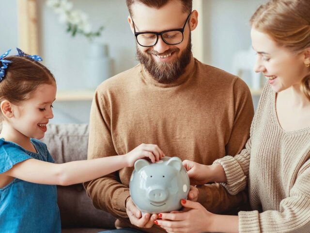 Mother and father watch young daughter put money into piggy bank 978b8d064138018a1dfad71b9882dd21