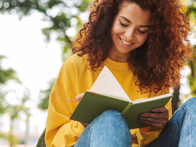 Young female college student writes in notebook while sitting outside on campus 978b8d064138018a1dfad71b9882dd21