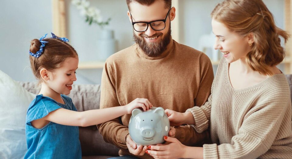 Mother and father watch young daughter put money into piggy bank 978b8d064138018a1dfad71b9882dd21