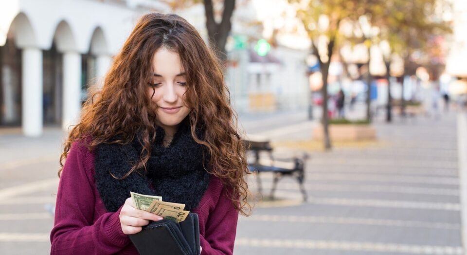 Young woman smiles as she puts money back in her wallet 978b8d064138018a1dfad71b9882dd21