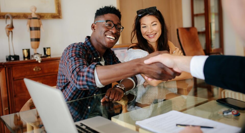 Young couple shake hands with closing agent at house closing meeting 978b8d064138018a1dfad71b9882dd21