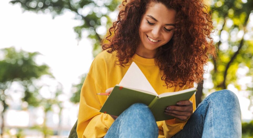 Young female college student writes in notebook while sitting outside on campus 978b8d064138018a1dfad71b9882dd21